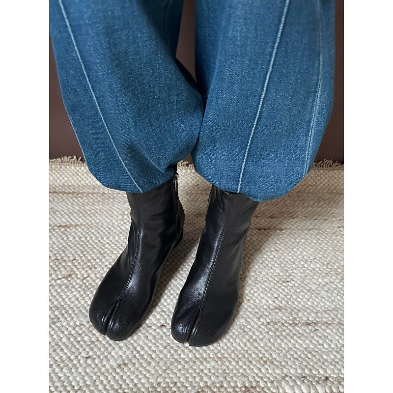 Black tabi-style ankle boots worn with blue jeans on a textured beige woven rug.