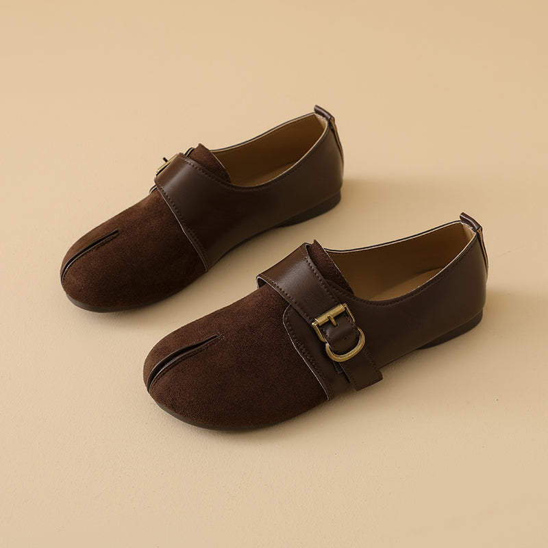 A pair of dark brown split-toe Mary Jane shoes with a suede-like finish and a leather strap featuring a gold buckle, displayed on a warm beige background.