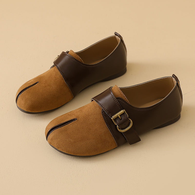 A pair of women's split-toe flat shoes with a tan suede lower and dark brown leather upper strap, featuring a gold buckle and a vertical slit detail, set against a solid beige background.