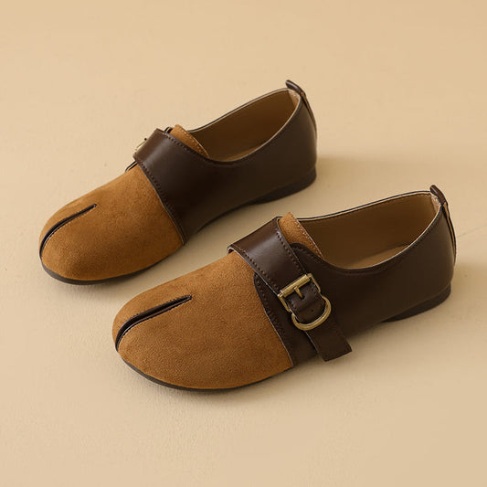 A pair of women's split-toe flat shoes with a tan suede lower and dark brown leather upper strap, featuring a gold buckle and a vertical slit detail, set against a solid beige background.