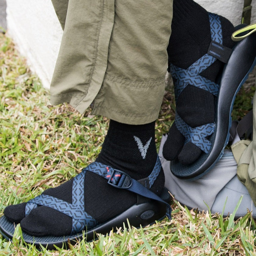Close-up of black V-Toe wool-blend split-toe tabi socks worn on the feet with Blue loop strap Sandals.